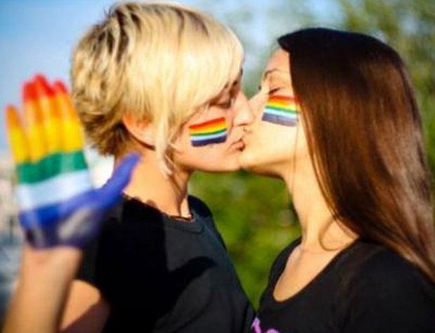 Dos mujeres se besan con la bandera del arcoíris.