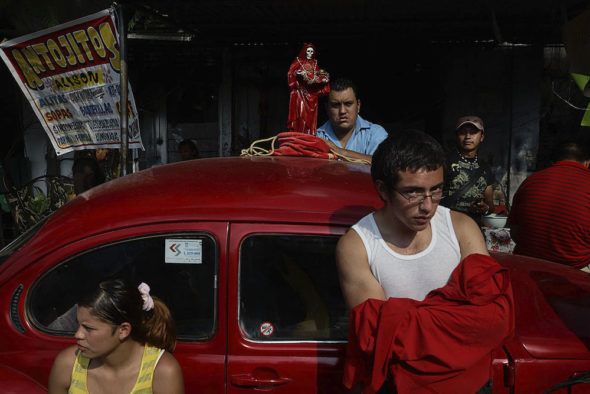 Tepito, México. Los devotos de la Santa Muerte se paran junto a un Vocho rojo (Escarabajo Volkswagen) estacionado fuera del santuario de la santa, esperando la misa mensual en su honor. Foto: Adriana Zehbrauskas.