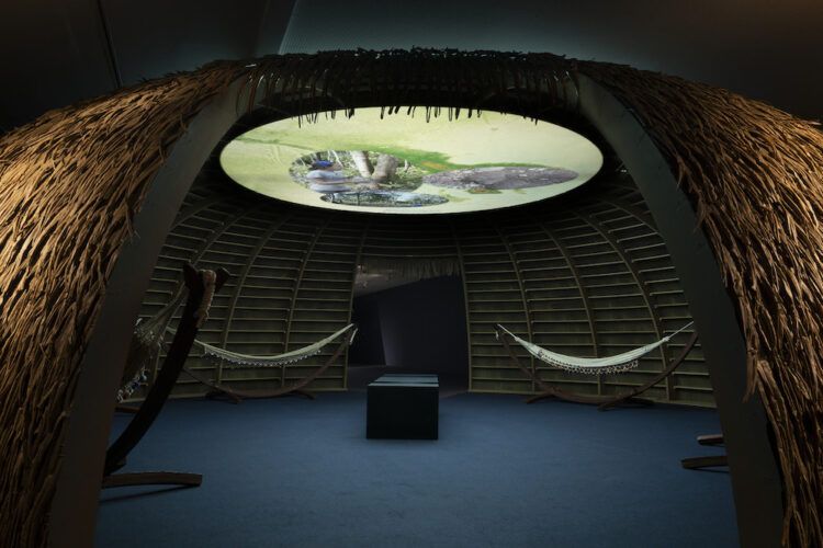 Videoinstalación (color, sonido) con madera, hojas de palmera, hamacas tradicionales de algodón tejido a mano kali’na de la Guayana Francesa 61 min. Tabita Rezaire. Nebulosa de la calabaza, 2024. Museo Nacional Thyssen-Bornemisza, Madrid. Foto: Roberto Ruiz, TBA21 Thyssen-Bornemisza Art Contemporary.